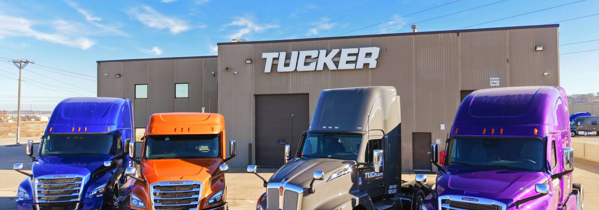 Blue, Orange, Grey and Purple Semi Trucks Parked In Front Of Tucker Freight Lines Terminal