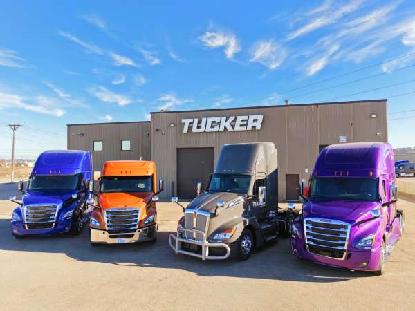 Blue, Orange, Grey and Purple Semi Trucks Parked In Front Of Tucker Freight Lines Terminal