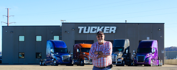 Diver standing in front of Tucker Freight Lines Terminal with Colorful Trucks Parked Behind Him