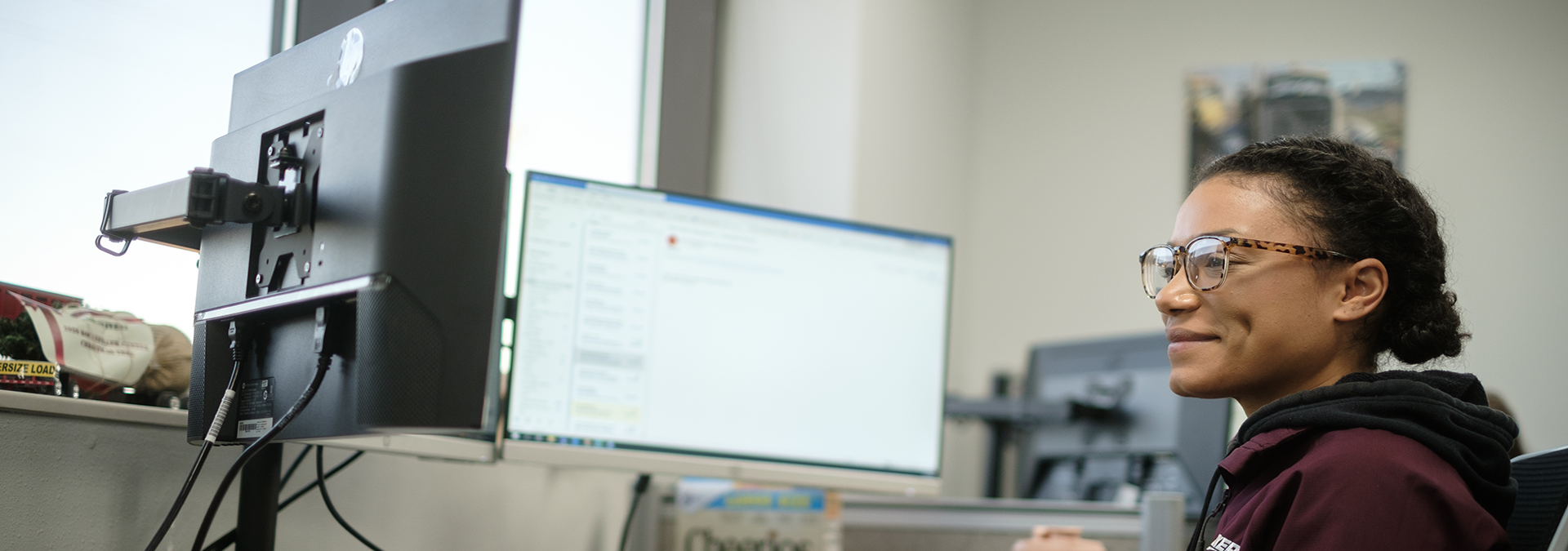 woman smiling while typing in front of double monitors