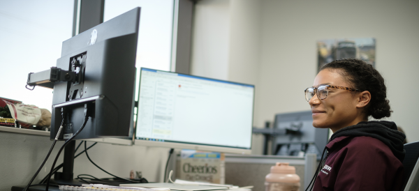 woman smiling while typing in front of double monitors